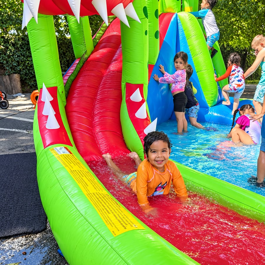 A child sliding down a dinosaur-themed inflatable water slide