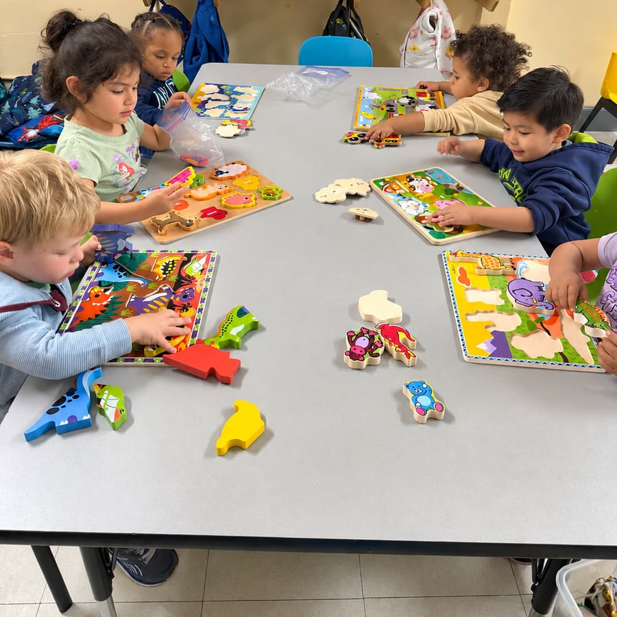 Children working on wooden puzzles together at a classroom table