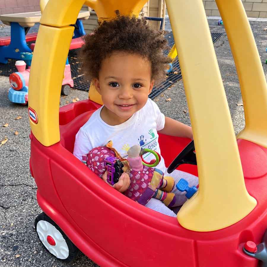 A smiling toddler sitting in a red and yellow toy car
