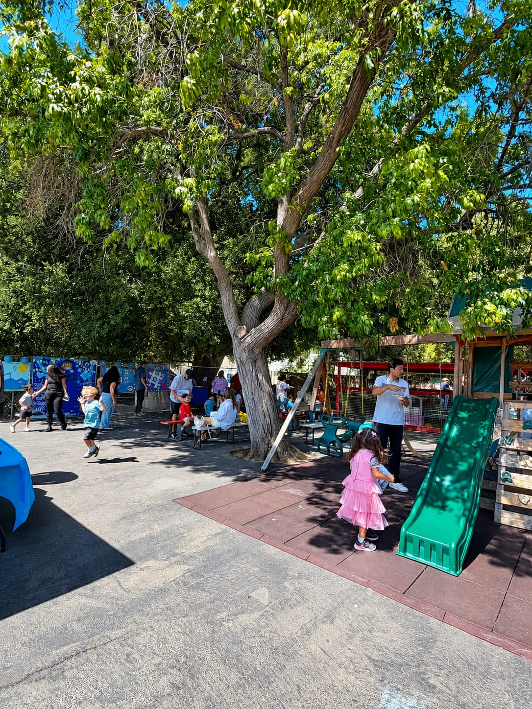 Children playing in the shaded play yard while a staff member looks on