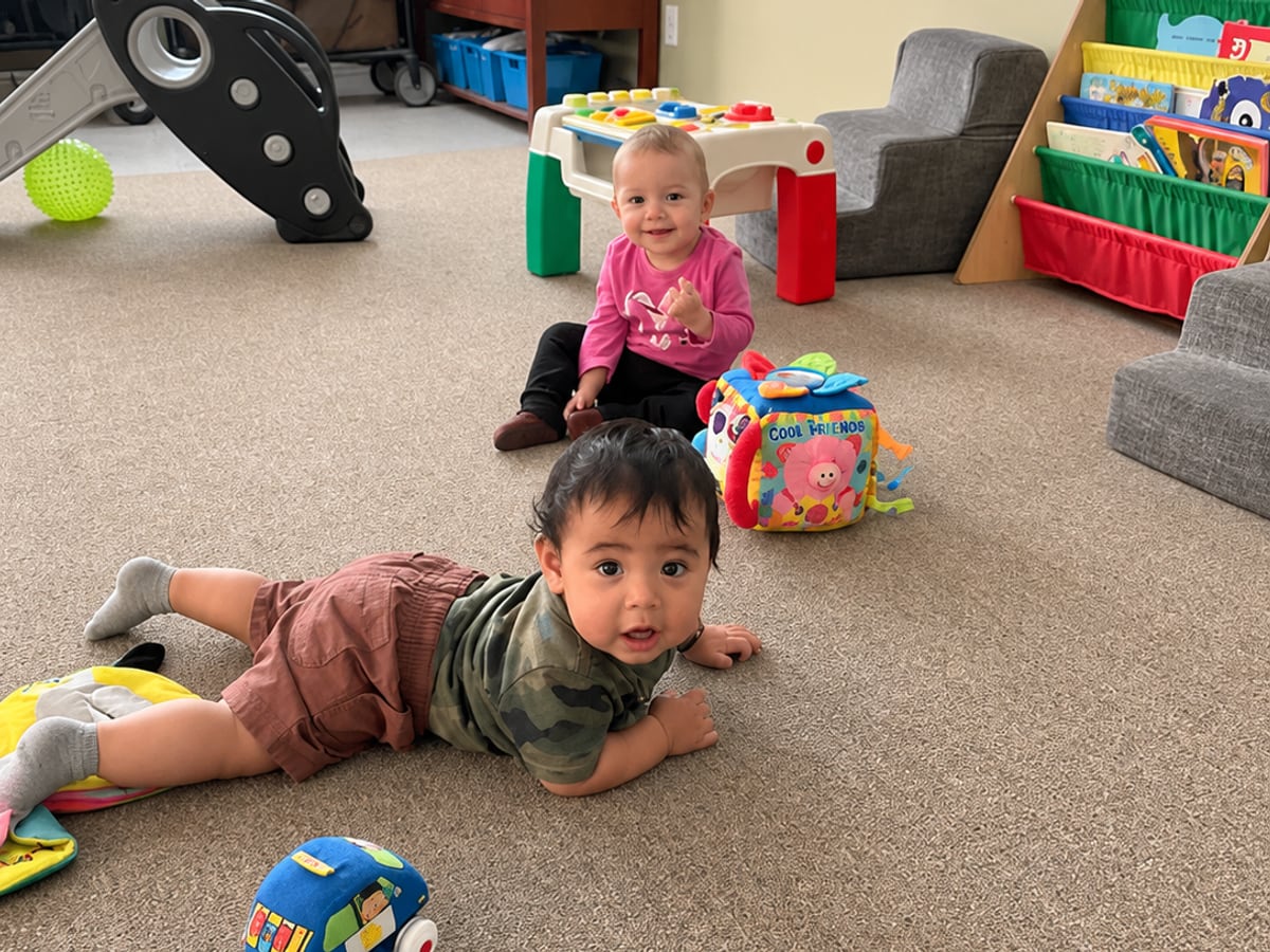 A baby playing on the floor with toys in the infant room