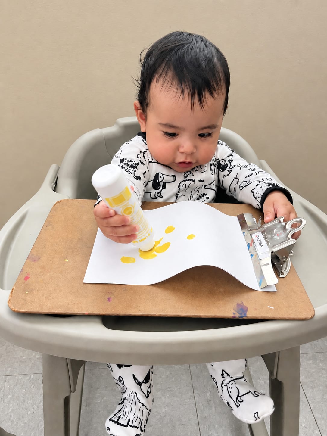 An infant in a high chair exploring a glue stick during a sensory art activity
