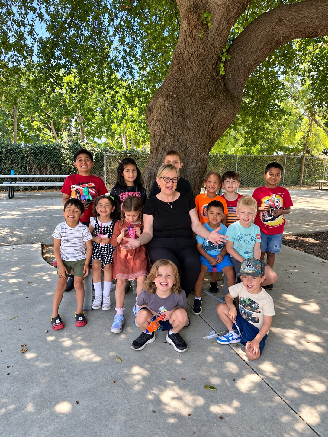 Director Robin Petrossian with a group of Pre-K students gathered under a shade tree on campus