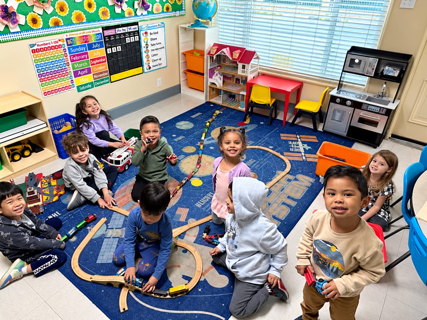 Two-year-olds gathered around a wooden train track set in the classroom