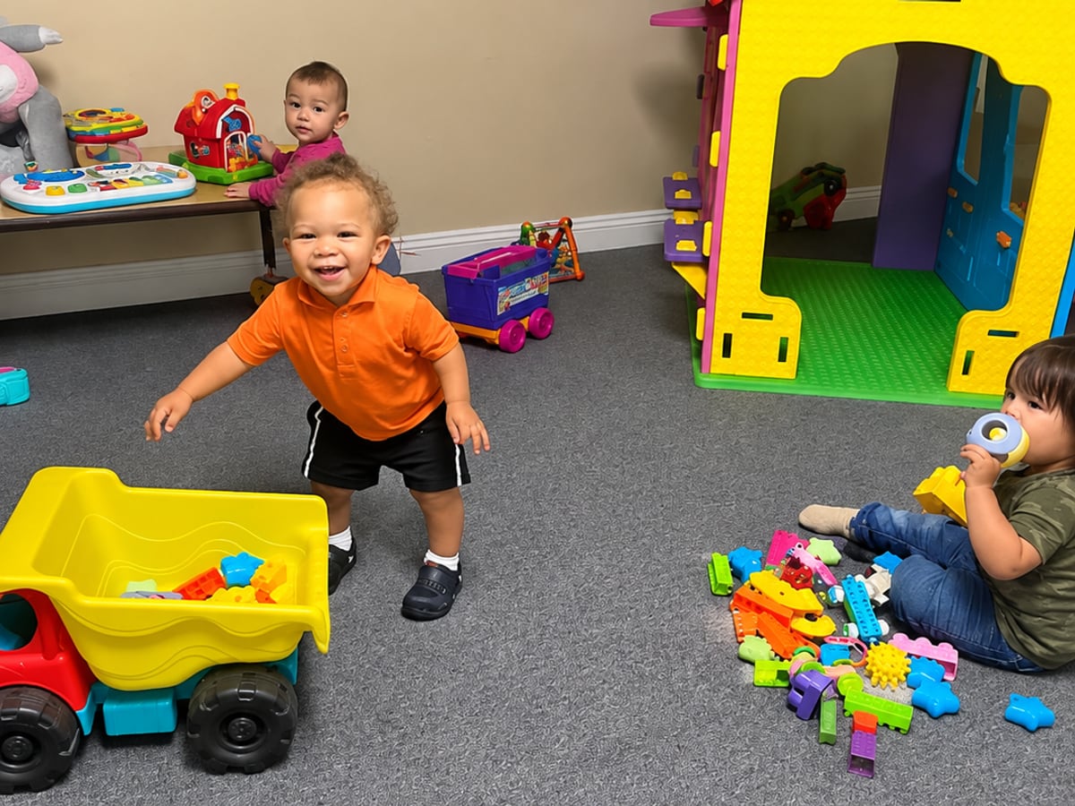 Toddlers playing with toys and a playhouse in the toddler room